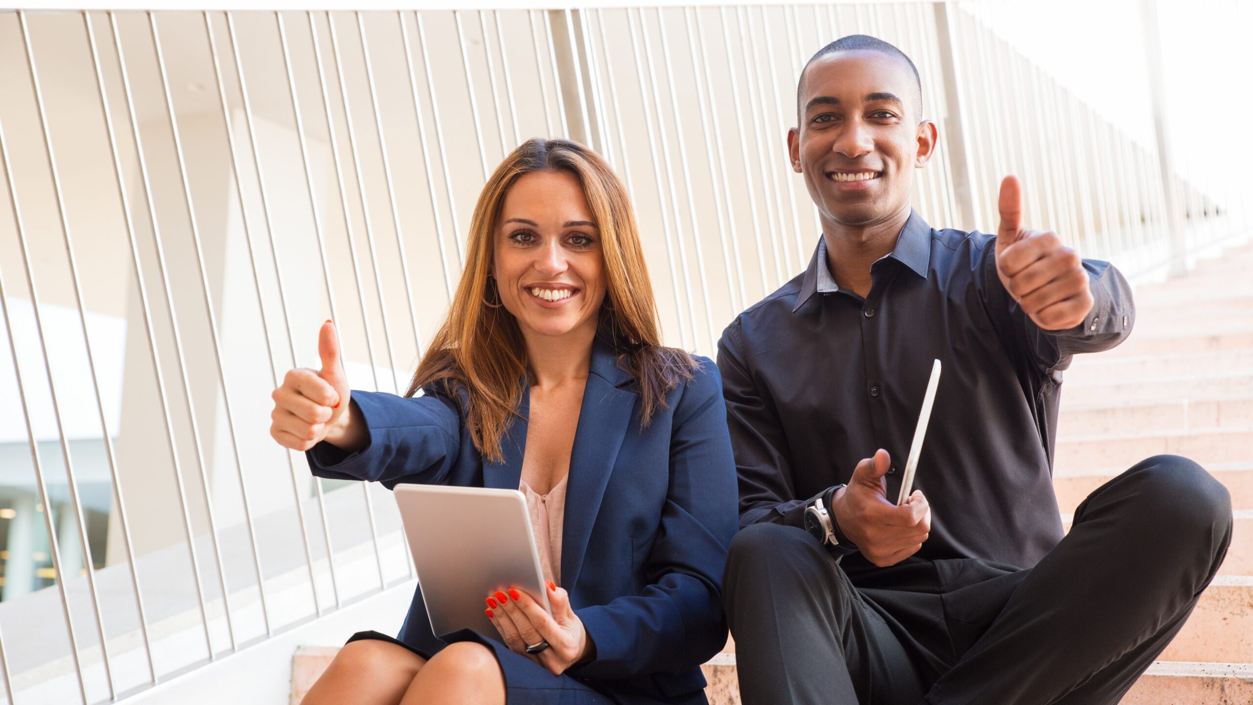 happy-coworkers-holding-tablets-showing-thumbs-up-stairs-morocco-business-goals