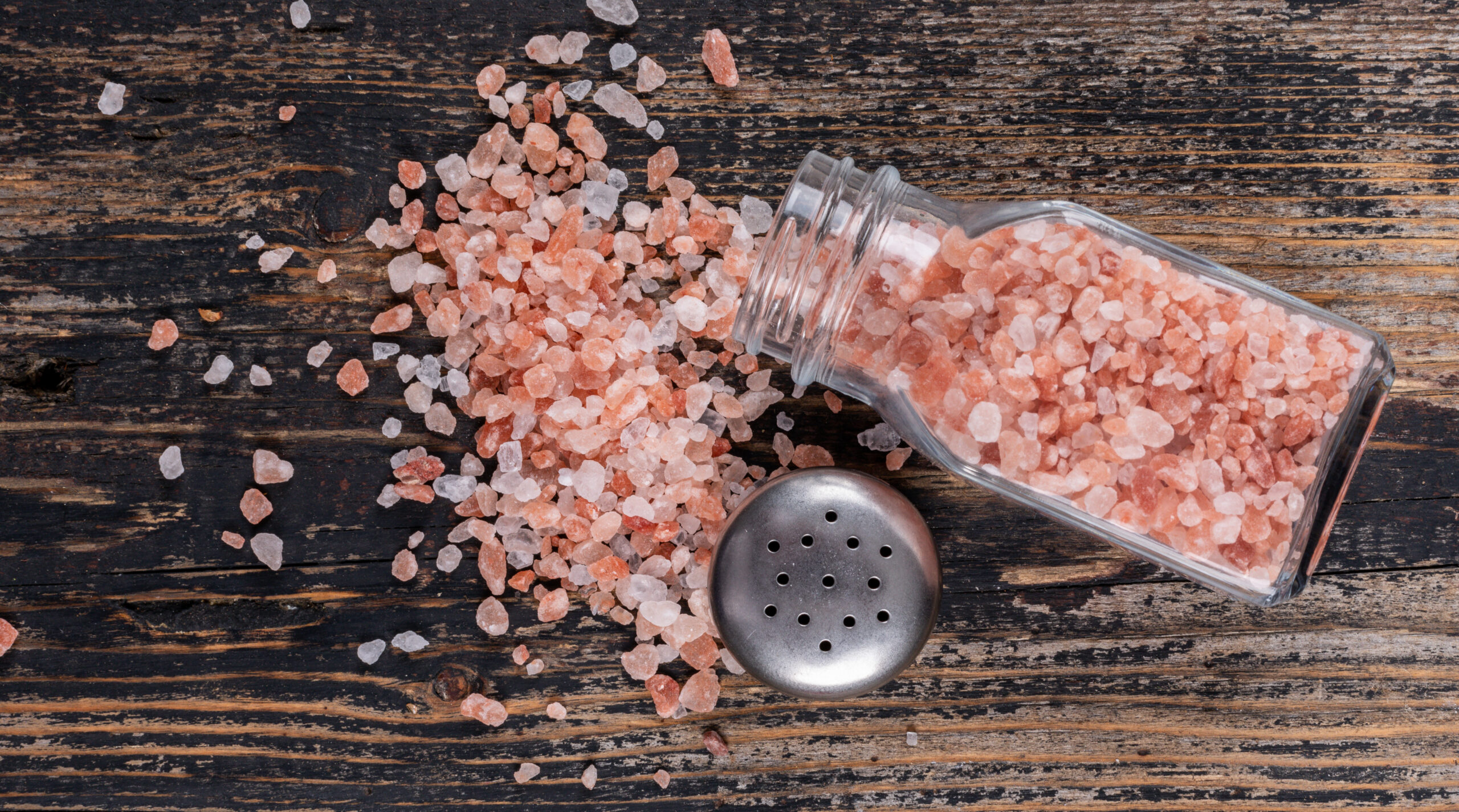 Himalayan salt coming out of open salt shaker on a dark wooden background top view
