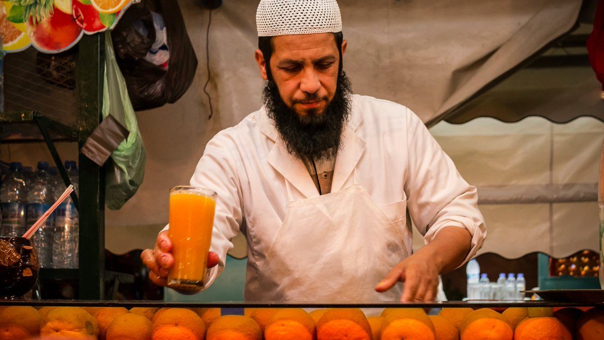 A vendor at a Moroccan market stall handing a glass of refreshing Moroccan drinks to a customer on a hot summer day