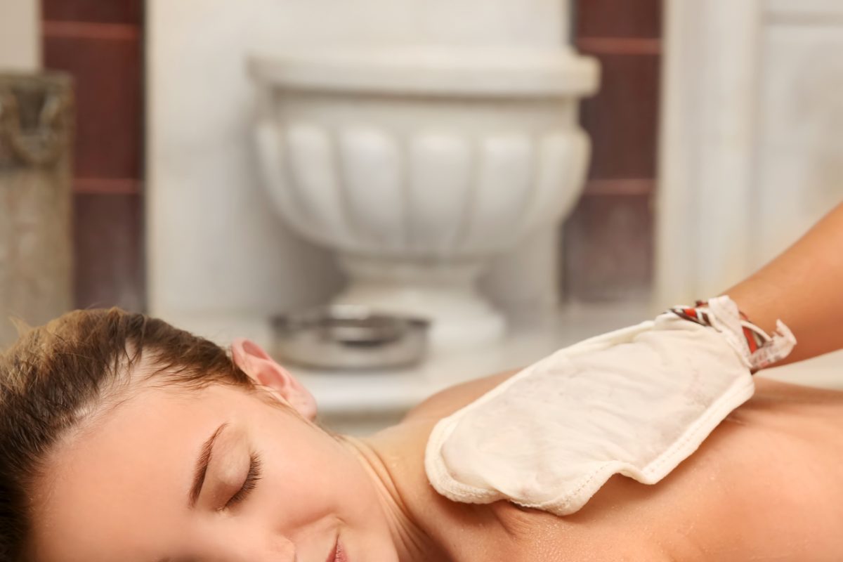 A skilled attendant performs hammam ritual exfoliation using a kessa glove on a client in a Moroccan wellness space.