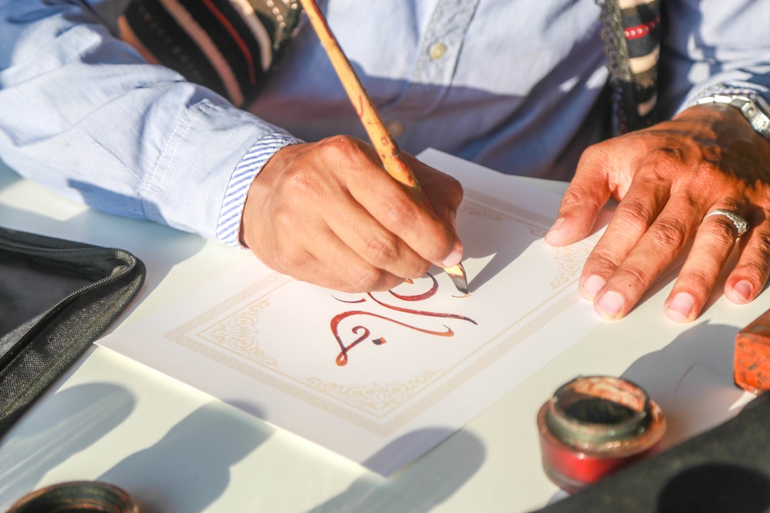 A Moroccan calligraphy artist holds a reed pen over paper covered in flowing Arabic script