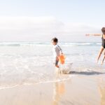 A mother and her children staying kids cool at a sunny Moroccan Atlantic beach, splashing in shallow waves near the shore.