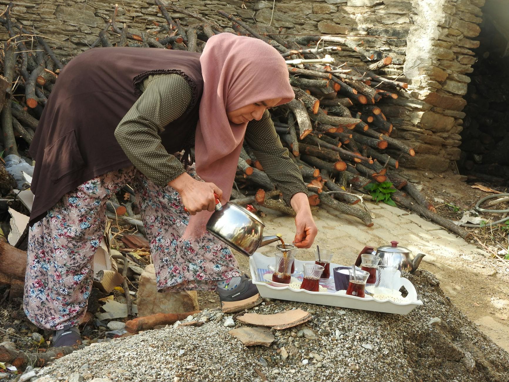 A woman in traditional dress pours Morocco mint tea from a silver teapot onto an ornate brass tray in a riad courtyard