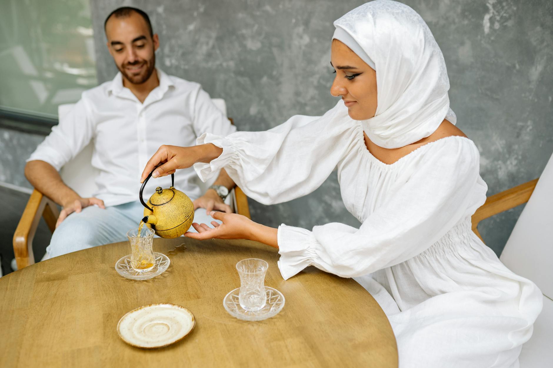 A man performs the high pour of Morocco mint tea into decorated glasses inside a sunlit medina tea room