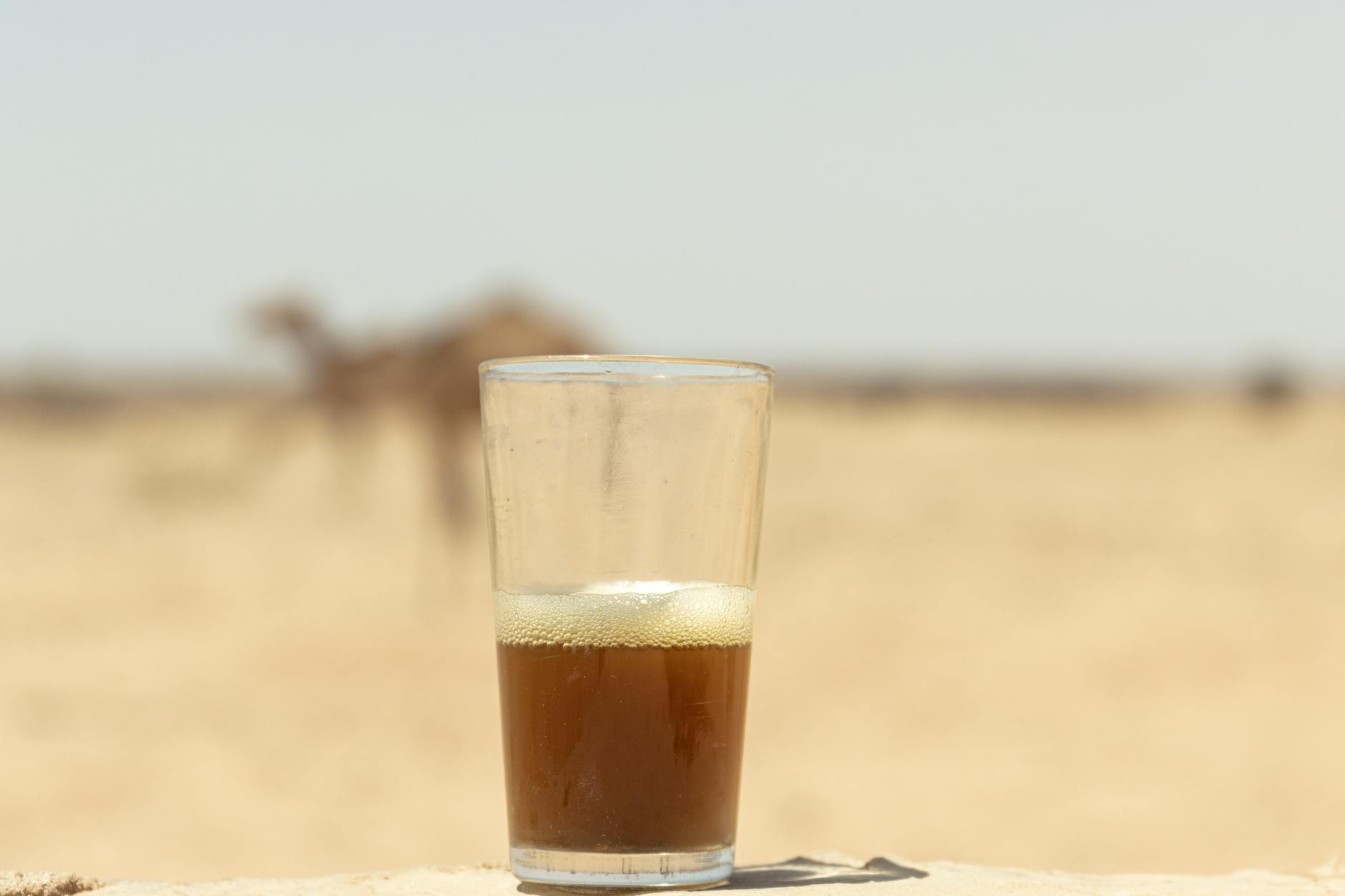 A traveler holds a small glass of Morocco mint tea at a Sahara desert camp as a Berber guide prepares the next round
