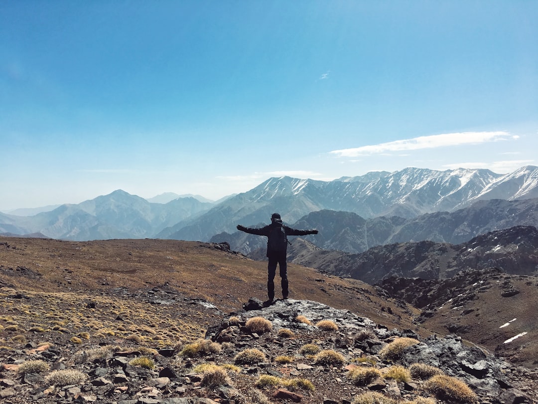 A hiker walks a mountain trail near Azilal at sunrise with High Atlas peaks in the background