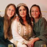A Moroccan family dressed in traditional djellabas gathering outdoors during Fête du Trône festivities in a city medina