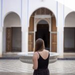 A woman sitting beside a central courtyard fountain in a traditional Moroccan riad, experiencing natural riad cooling.